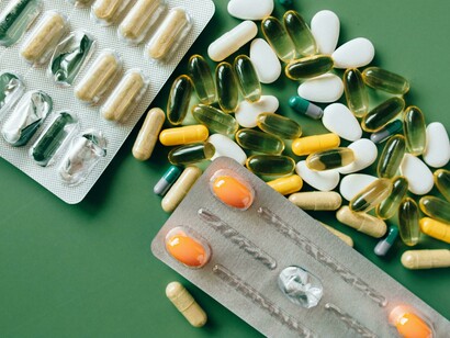 A photo of alternative medicines and multivitamins arranged with green leaves on a green table, blending nature with modern wellness