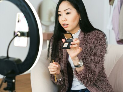 An influencer applying makeup while live streaming on her smartphone   Colleagues in aprons sitting on a staircase and browsing smartphones while scrolling through social media