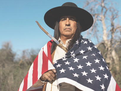 The image of a Native American man in the desert with an American flag highlights the contrasts and connections between American individualism and native identity