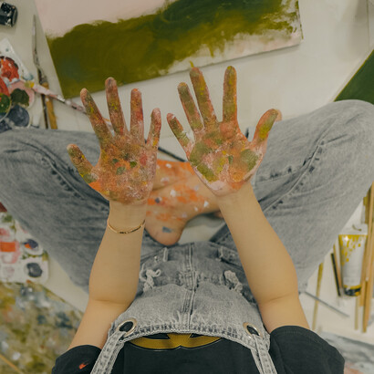 Criança olhando para as mãos sujas de tinta após terminar uma pintura em um quadro