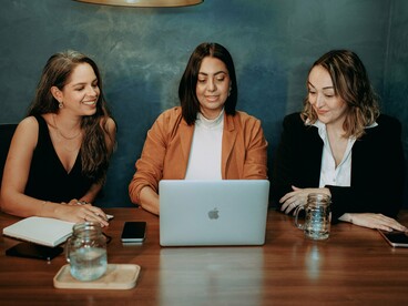 Three colleagues working together around a laptop, symbolizing a workplace built on cooperation, communication, and mutual respect