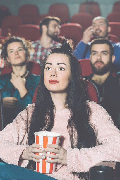 A brunette woman enjoying popcorn in a cinema, fully immersed in the movie theater experience