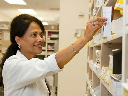 In the bustling pharmacy, a diligent female pharmacist carefully examines a medication from the well-organized inventory