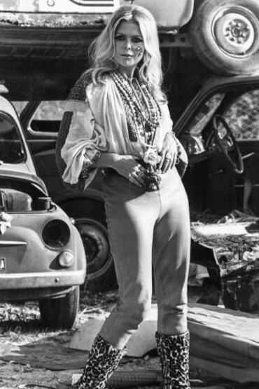 A hippie woman standing in front of vintage cars in the 1960s counterculture era