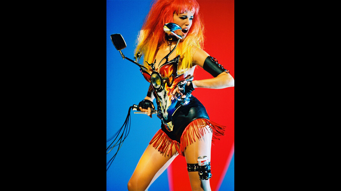 Patrice Stable, La mannequin Emma Sjöerg Wiklund lors du tournage du vidéoclip Too Funky de George Michael, Paris, 1992. Tenue : Thierry Mugler, collection Les Cow-boys, prêt-à-porter printemps-été 1992. Bustier « carénage de motocyclette » en plexiglas peint à la main (Jean-Jacques Urcun), cœur matelassé dans le dos. Short et franges en cuir. Jarretière « Budweiser » assortie. Photo : © Patrice Stable.