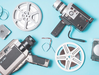 Against a blue backdrop, an overhead perspective showcases film strips, a film reel, and diverse camcorders, encapsulating the essence of cinematography and film production