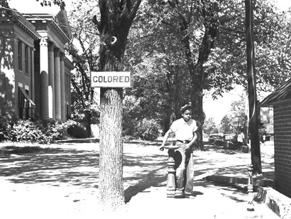 A young boy using a 'colored' only water fountain
