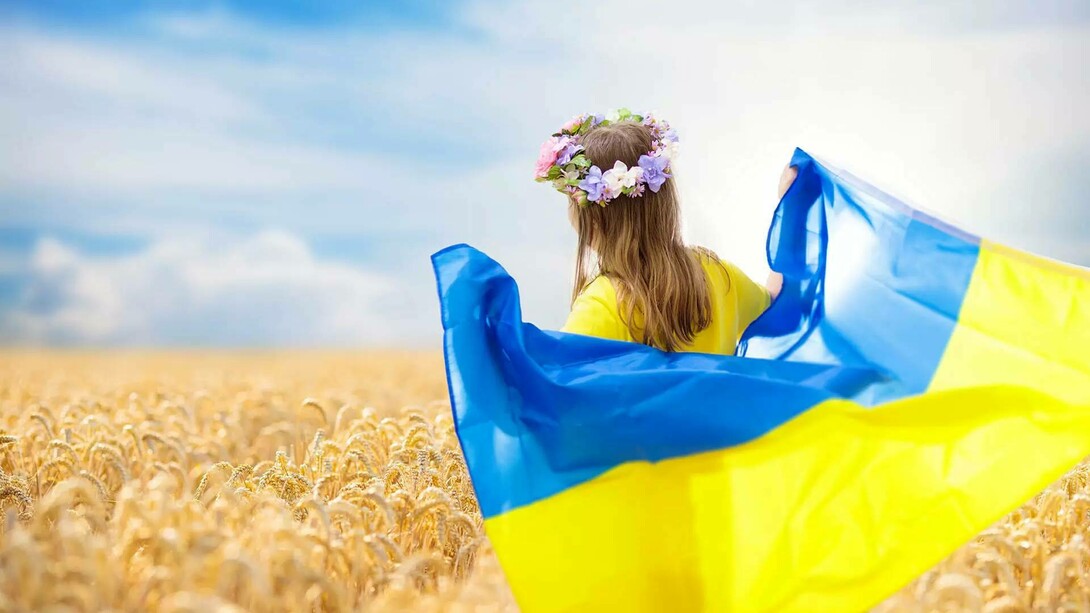 A young Ukrainian girl with a crown of flowers resting on her head carrying the Ukrainian flag as a hope for peace