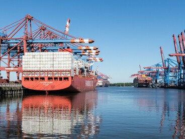 A massive container ship docked at a busy port, representing the global trade networks at the heart of economic power