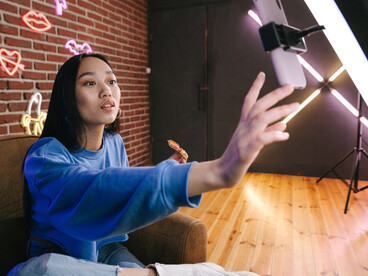 A young Asian woman livestreams from a neon-lit studio, engaging her audience through creative digital content and real-time interaction