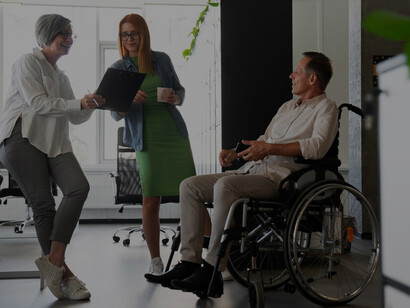 A man in a wheelchair working at his office job, surrounded by a diverse group of colleagues, highlighting inclusion and teamwork