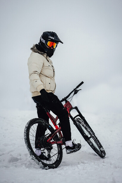 A man dressed in a beige jacket cycling a red mountain bike over the snowy terrain of Jammu & Kashmir, India, on a clear daytime