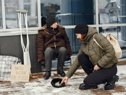 Homeless man seeking food on a winter city street as a woman offers help