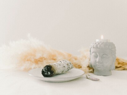 A sage burning with a Buddha candle head shows Ayurvedic detox rituals like abhyanga