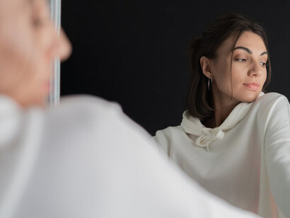 A young woman in a white hoodie posing in front of a mirror, capturing a moment of self-discovery and self-reflection