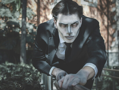 A dramatic Gothic-style portrait featuring a man with makeup, set in a sunlit scene