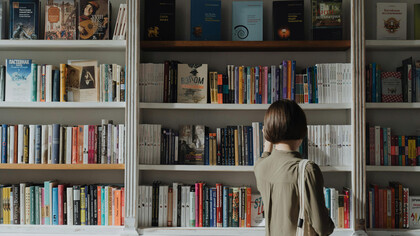 Una joven revisando una biblioteca, a punto de reencontrarse con la necesaria reedición de una obra