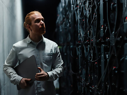Technician holding a laptop and monitoring an LED wall display in a server room