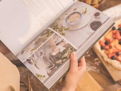 Capture the essence of home cooking as a woman consults a cookbook while preparing a meal in her kitchen, embodying the art of culinary exploration and creativity