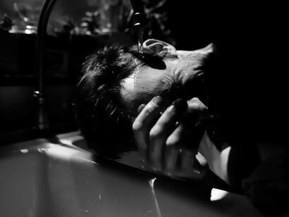 A compelling visual unfolds as a man finds himself submerged beneath the cascading stream of water from a tap, symbolizing a profound connection with the elemental force and the fluidity of our existence