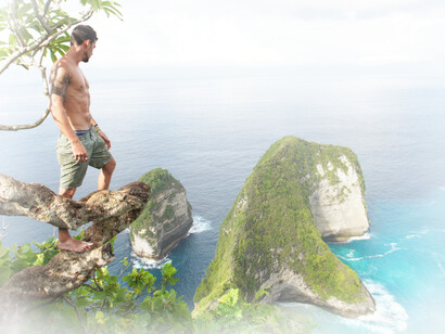 A man stands on a tree overlooking the beauty of the ocean while thinking