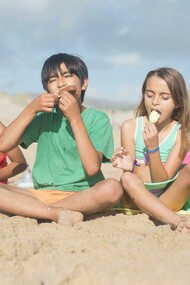 Children sitting on the sand in Portugal, enjoying ice cream sticks