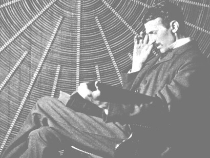 Tesla sitting in front of a spiral coil used in his wireless power experiments at his East Houston St. laboratory