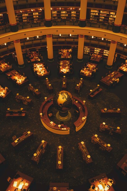Uma biblioteca monumental abriga corredores repletos de livros e um globo no centro do salão. A imagem remete diretamente ao universo infinito imaginado por Borges em “A Biblioteca de Babel”