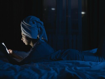 A woman using her phone while resting on her bed at night, conveying the blurred boundary between rest and digital compulsion