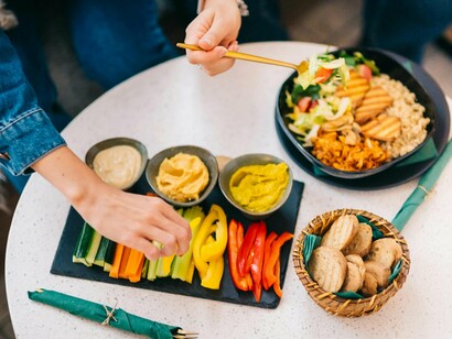 Na foto aparece as mãos de duas pessoas comendo alimentos feitos a partir de produtos de origem vegetal
