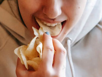 The girl is enjoying potato chips with her hands
