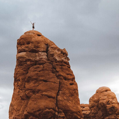 Escalador comemora no topo de uma enorme pedra ao chegar ao topo