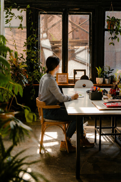 Sentada diante da mesa de trabalho, a mulher observa o espaço silencioso ao redor. Mesmo em tempos turbulentos, persistem lugares de criação, reflexão e reinvenção. A luminosidade suave do ambiente acompanha a mulher em sua rotina de trabalho. Pequenos instantes de serenidade ainda resistem às tempestades narrativas do presente