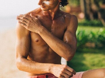 A man carefully covering exposed skin with sunscreen, symbolizing preventive care against harmful ultraviolet exposure