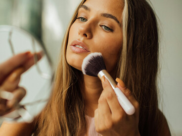 Close-up of a woman holding a makeup brush and mirror as she prepares for the day