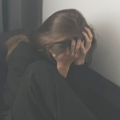 Tears glisten on a woman's cheeks as she leans against the wall, overcome with emotion