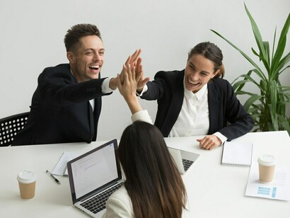 An excited millennial office team exchanging high fives, symbolizing team collaboration, workplace equity, and inclusivity within a multicultural workforce
