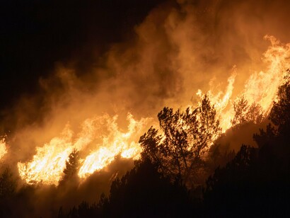 A wildfire consuming vast stretches of woodland, reflecting the mounting consequences of unsustainable development