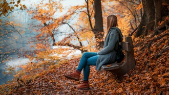 A woman sitting quietly on a bench surrounded by autumn leaves, representing the beauty of embracing a slower, simpler life