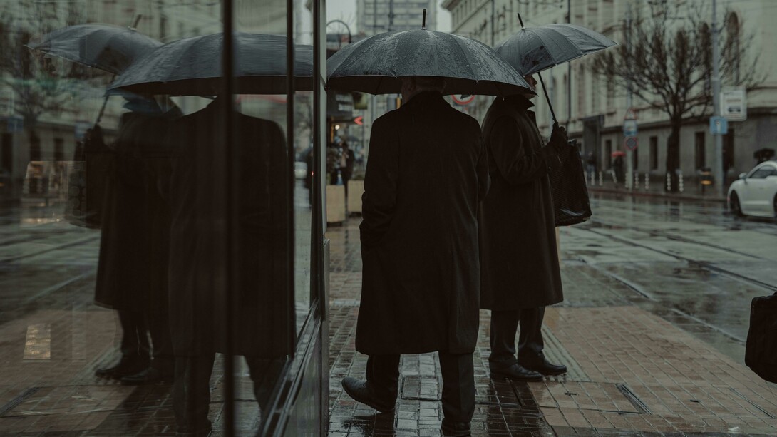Reflection of pedestrians carrying umbrellas in a glass window facade, Bulgaria