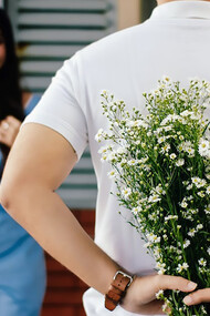 A man stands before a woman near a marble wall, tenderly presenting a bouquet of flowers, creating a scene of timeless romance
