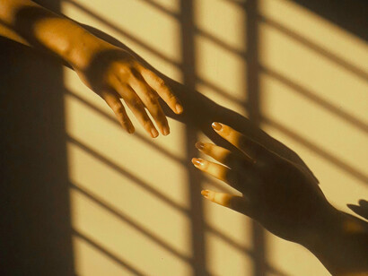 Traversant une zone d'ombres et de lumières, deux mains symbolisant l'accompagnement cherchent un équilibre entre emprise et détachement