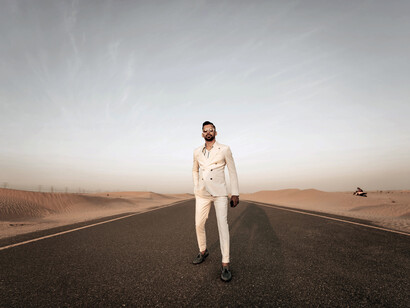 Dubai, United Arab Emirates. A man in a beige suit stands on the desert sand