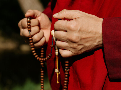 The hands of a person in a red cloak holding prayer beads