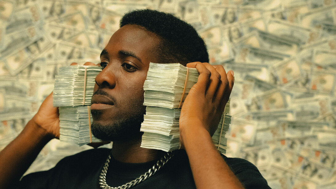 Un homme posant avec des piles d'argent liquide, mettant en valeur la concentration et l'état d'esprit de la génération actuelle issue du capitalisme