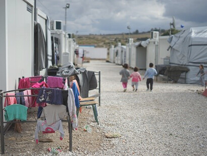 During the daytime, a multitude of people walk through a migration camp, their determined footsteps echoing a collective journey filled with hope and uncertainty