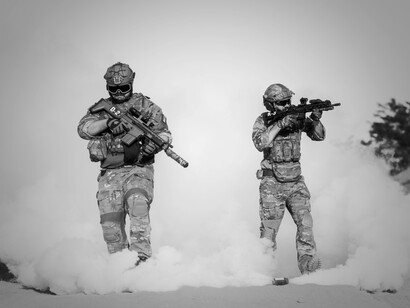 Black and white picture of two armed soldiers emerging from a smoke cloud, one of them aiming his rifle