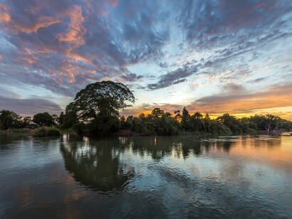 Nubes de colores y cielo azul con el reflejo en el agua de una isla cubierta de árboles al amanecer en Si Phan Don, Laos