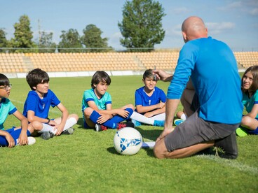 A youth football coach guiding his players in a huddle, reflecting the value of encouragement over evaluation