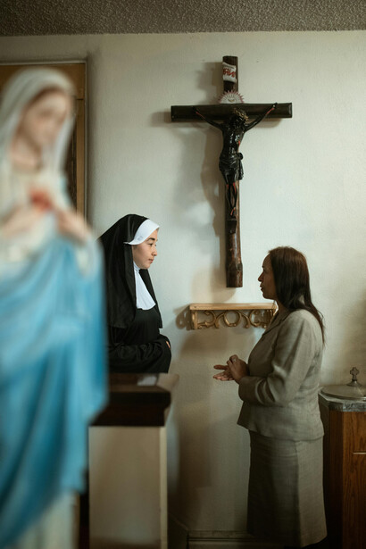 Mujer conversando con una monja, con una figura de la Virgen en primer plano